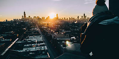 Photo of a person in a woolly hat and parka staring out at a Chicago sunrise.