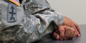 Closeup of a uniformed service member's hands folded on a table.